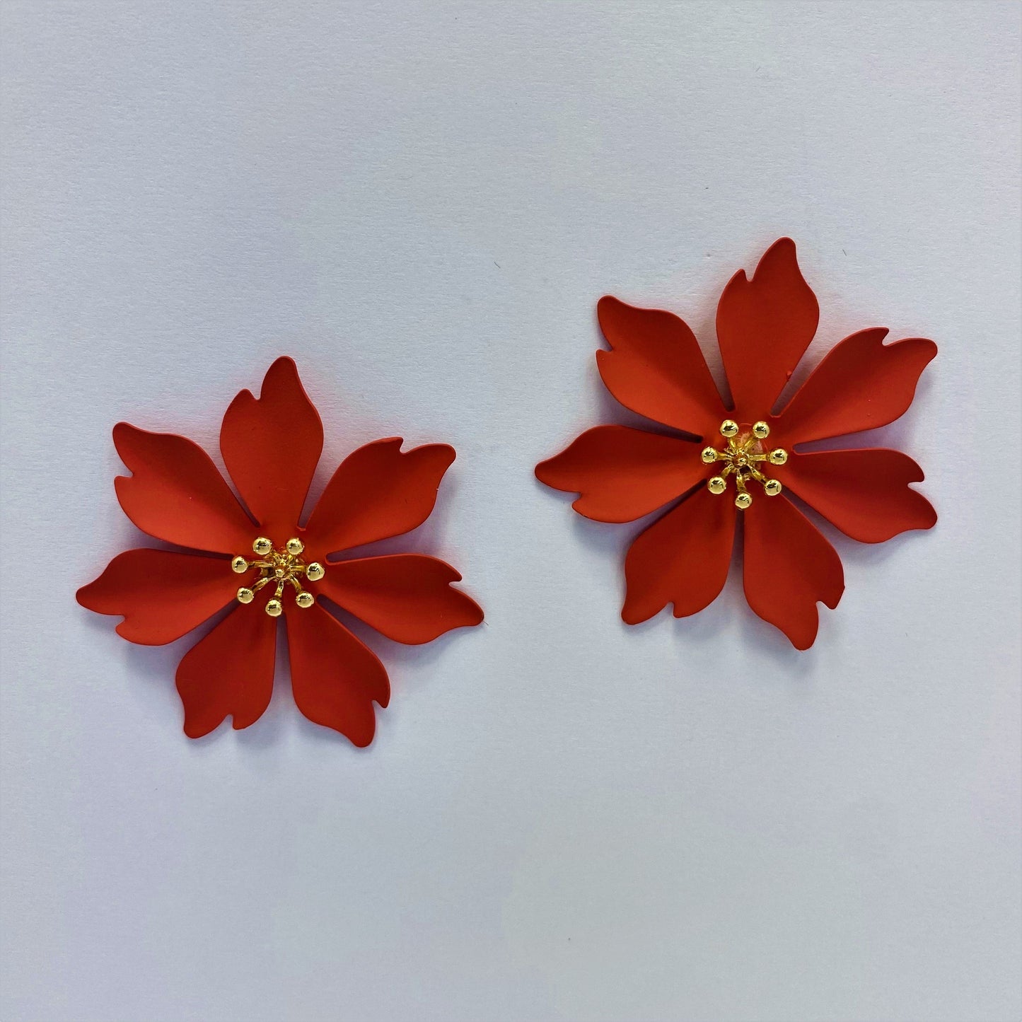 A collection of metal flower design stud style post earrings in various colors displayed on a mannequin ear and against a white background.