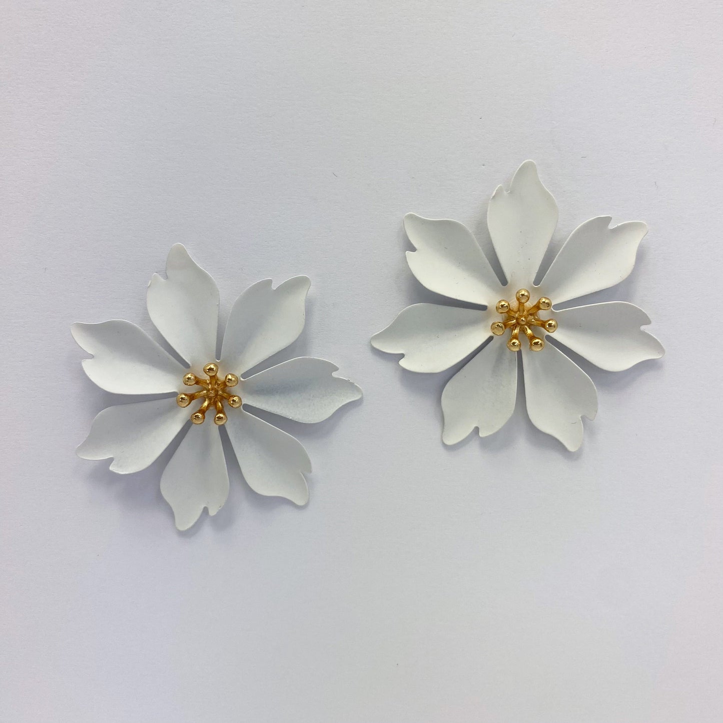A collection of metal flower design stud style post earrings in various colors displayed on a mannequin ear and against a white background.