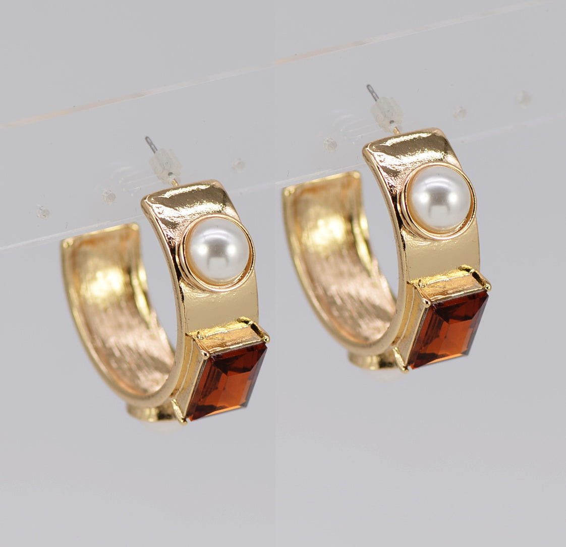 Gold hoop earrings with pearls and red gemstones on a light gray background
