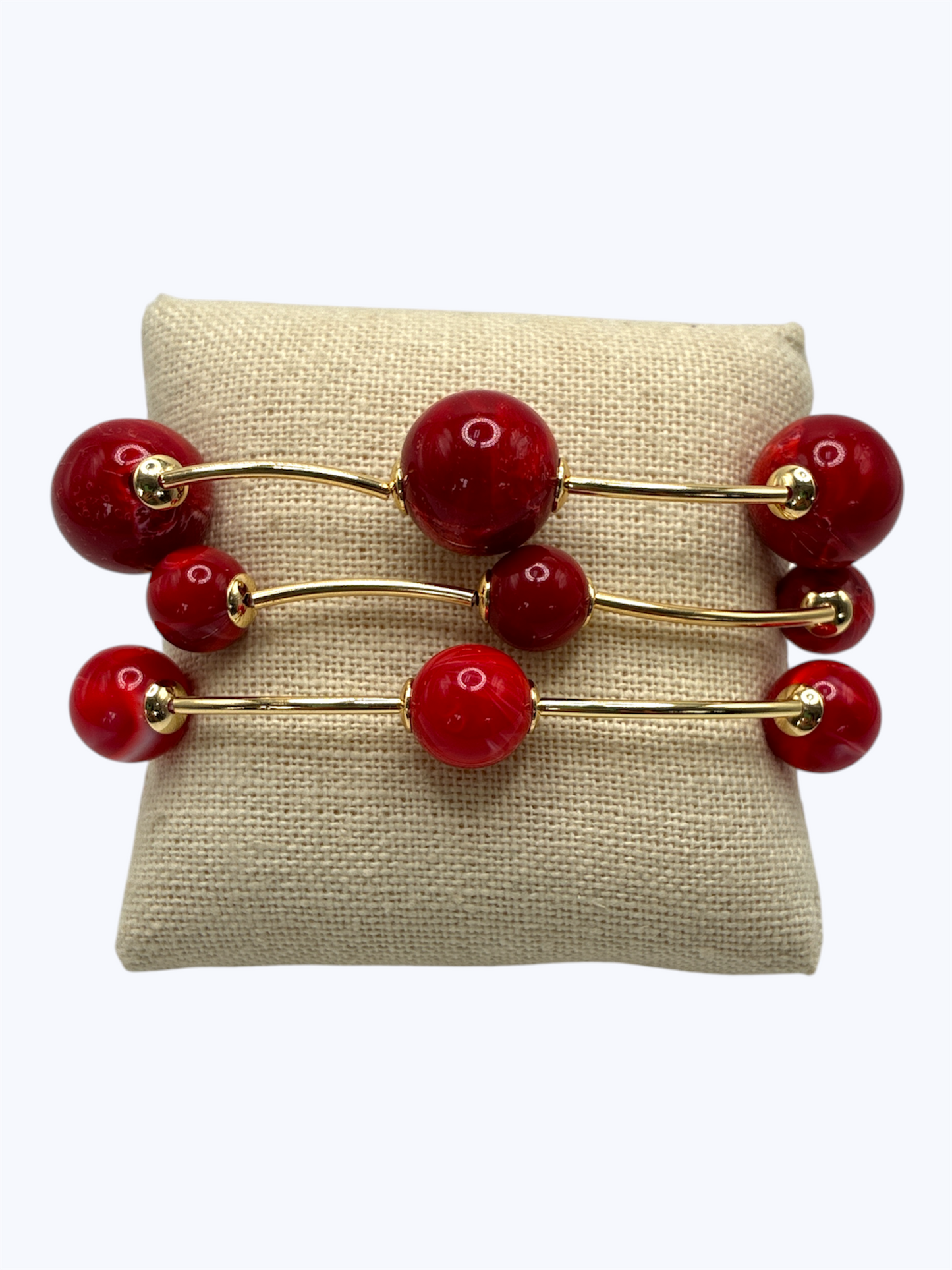 Elegant beaded stretch bracelet set with glossy round beads and gold-tone curved bar accents displayed on linen cushion for boutique fashion accessories collection