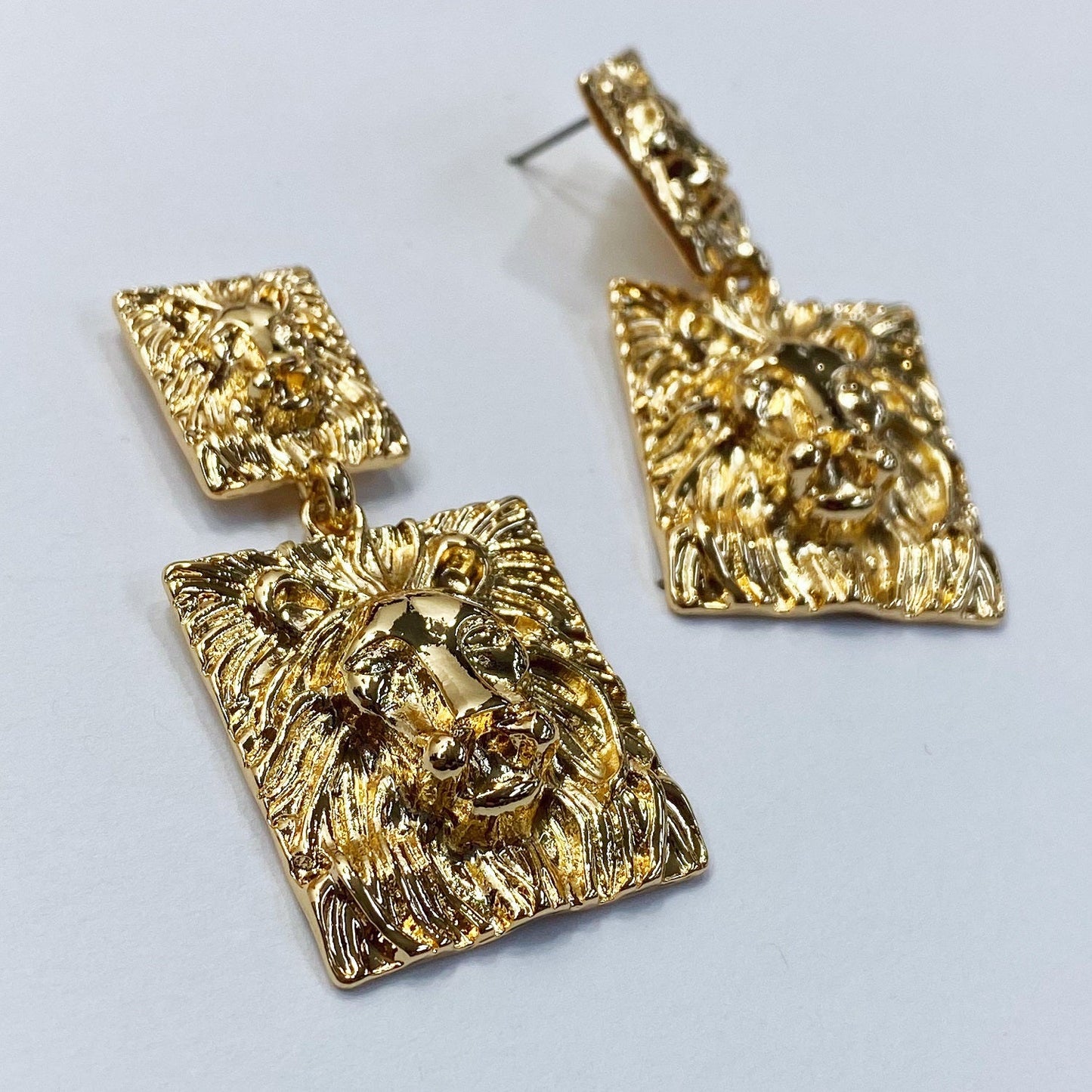 A pair of earrings which is lion-inspired on a white background