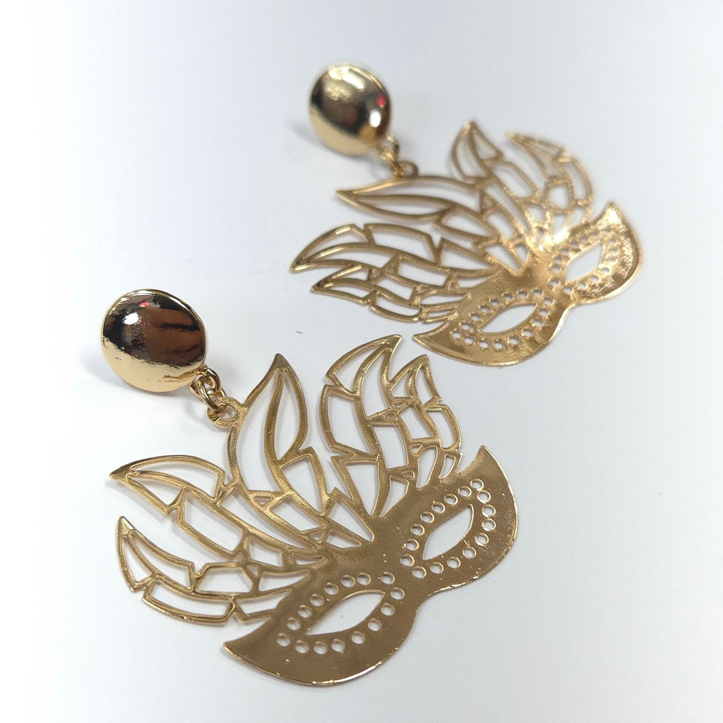 Gold mask-shaped earrings on a white background