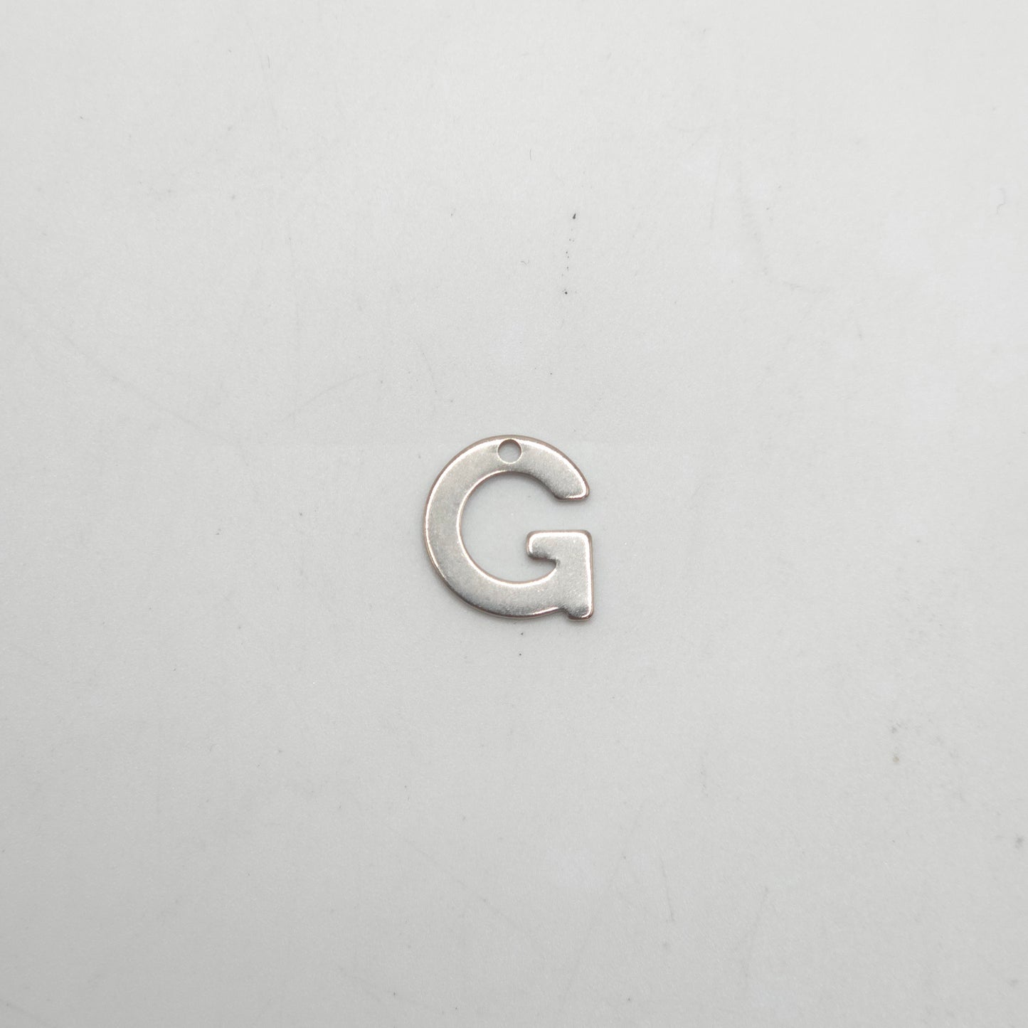 Silver letter 'G' charm on a light gray background