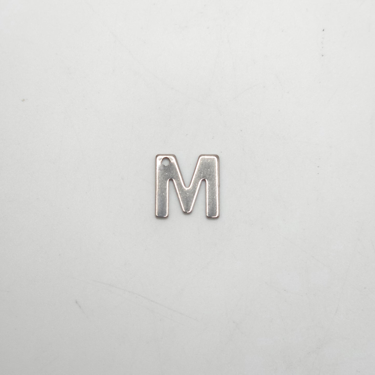Silver letter 'M' charm on a light gray background