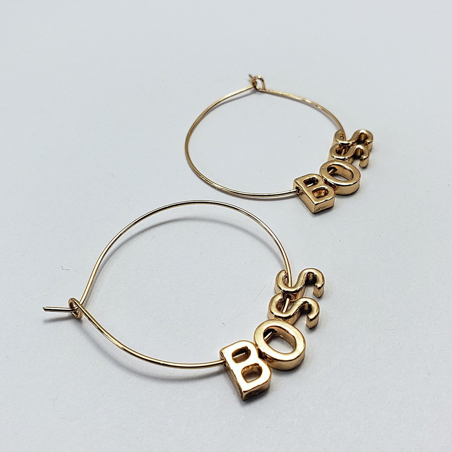 A pair of gold-colored hoop earrings with the word 'BOSS' written in a retro font, displayed in three different views on a white background.