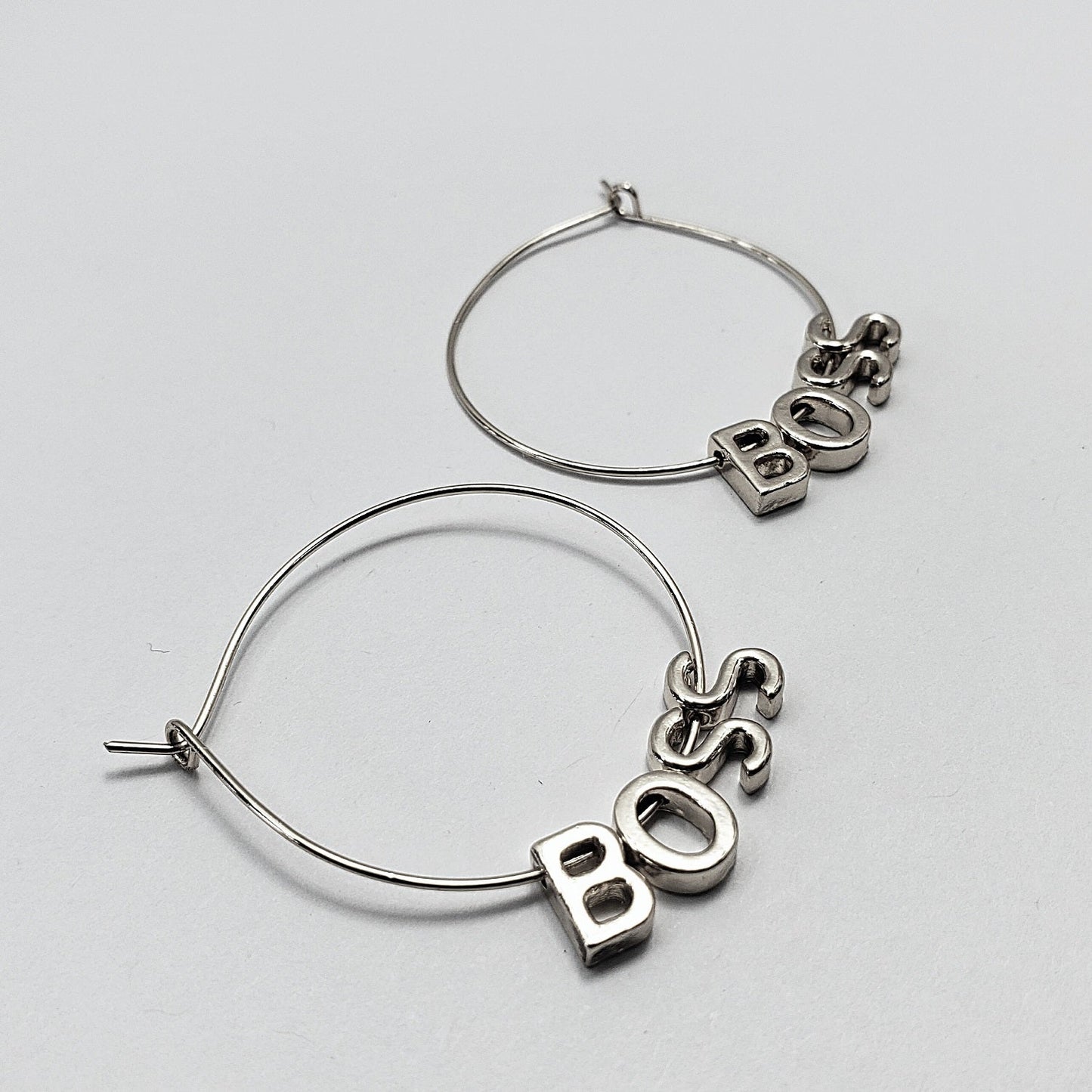 A pair of silver-colored hoop earrings with the word 'BOSS' written in a retro font, displayed in three different views on a white background.