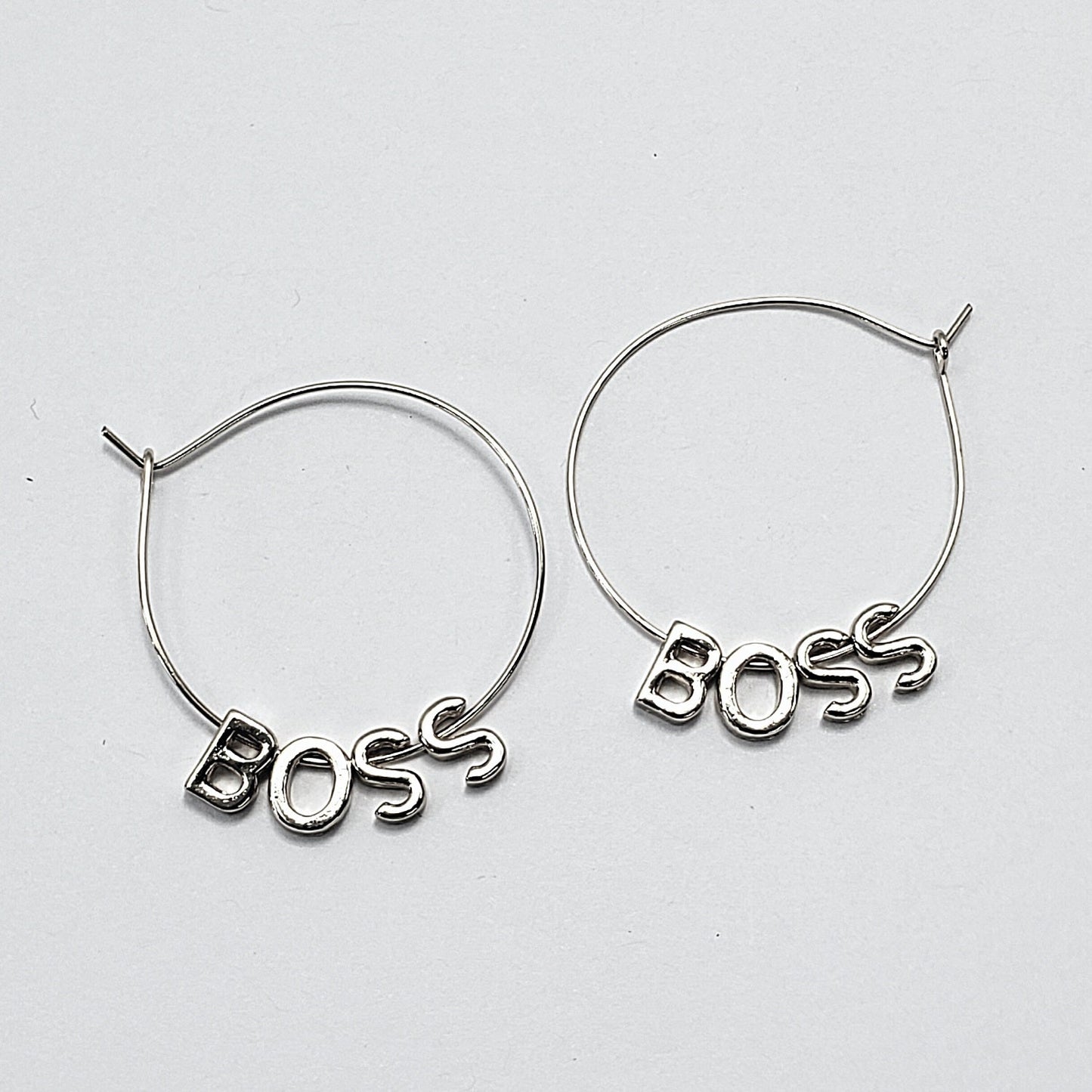 A pair of silver-colored hoop earrings with the word 'BOSS' written in a retro font, displayed in three different views on a white background.