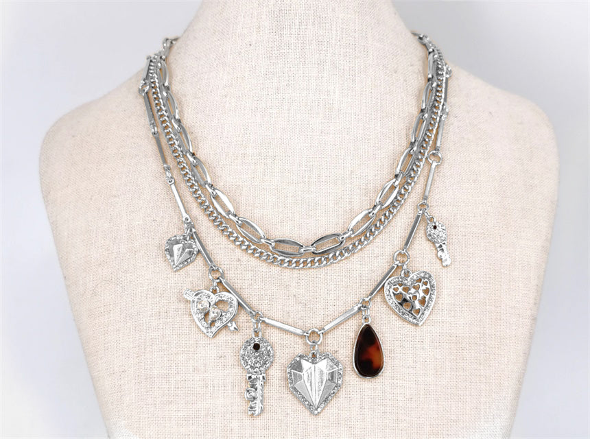 Multi-layered silver necklace with various charms on a mannequin bust.