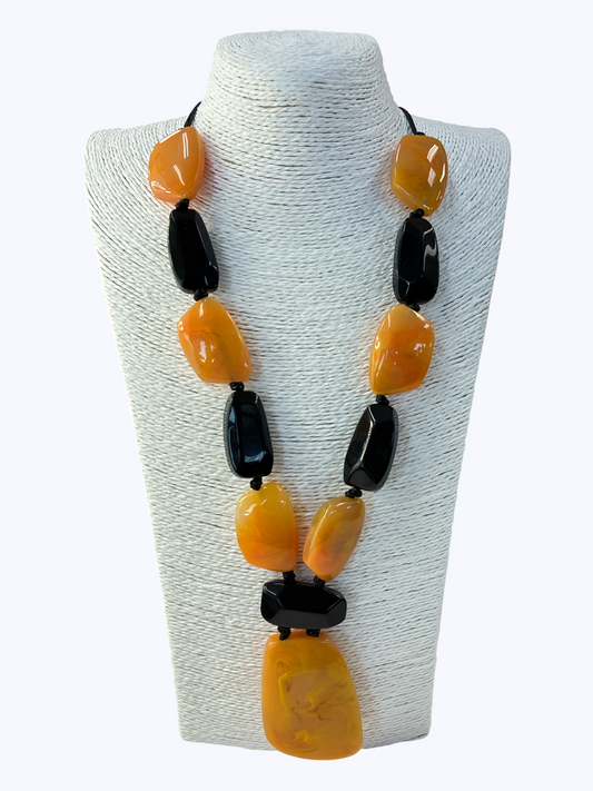 Chunky statement necklace with large amber-style and black resin beads in an alternating geometric design displayed on a mannequin bust