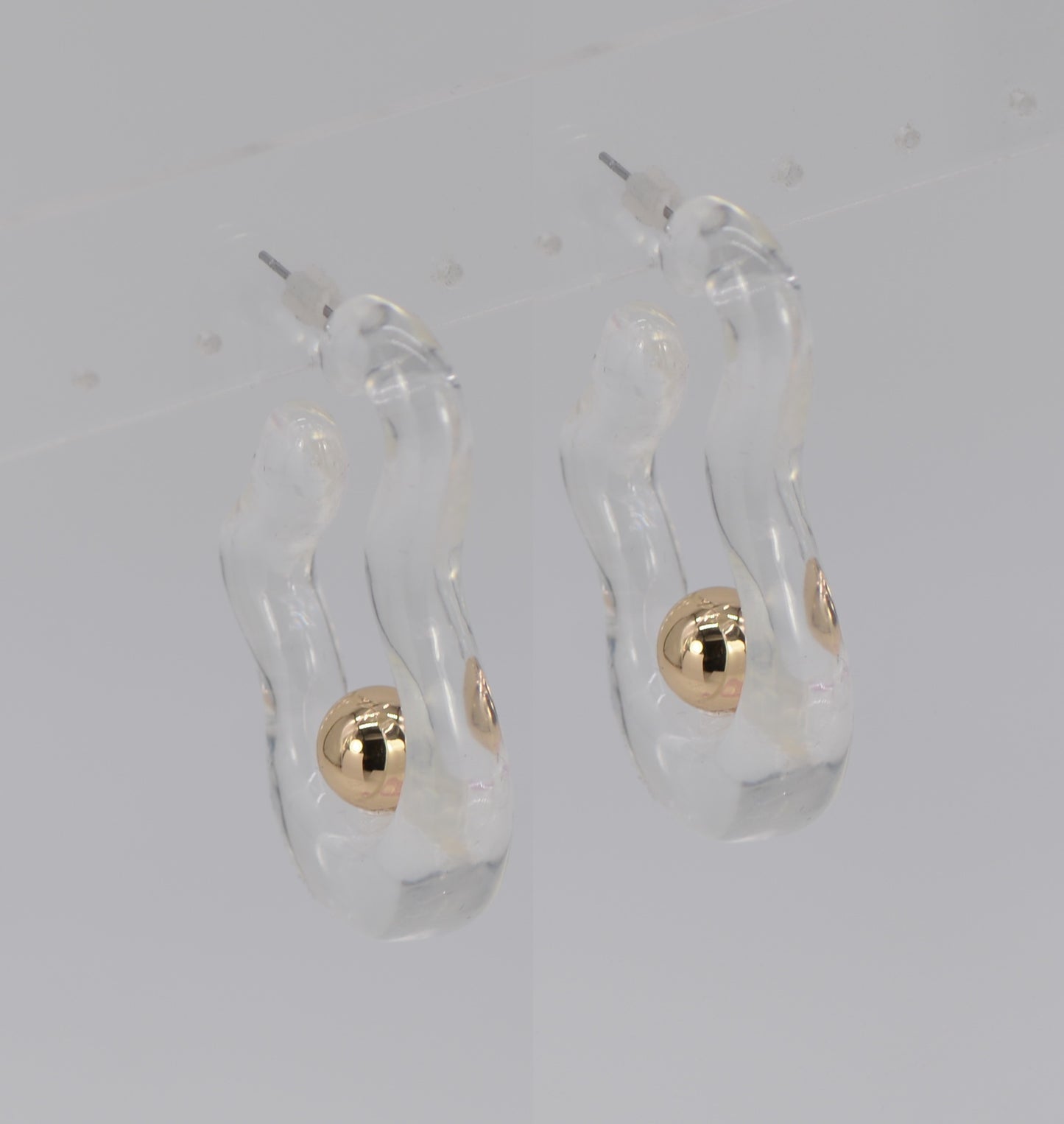 Clear earrings with gold spherical accents on a light gray background