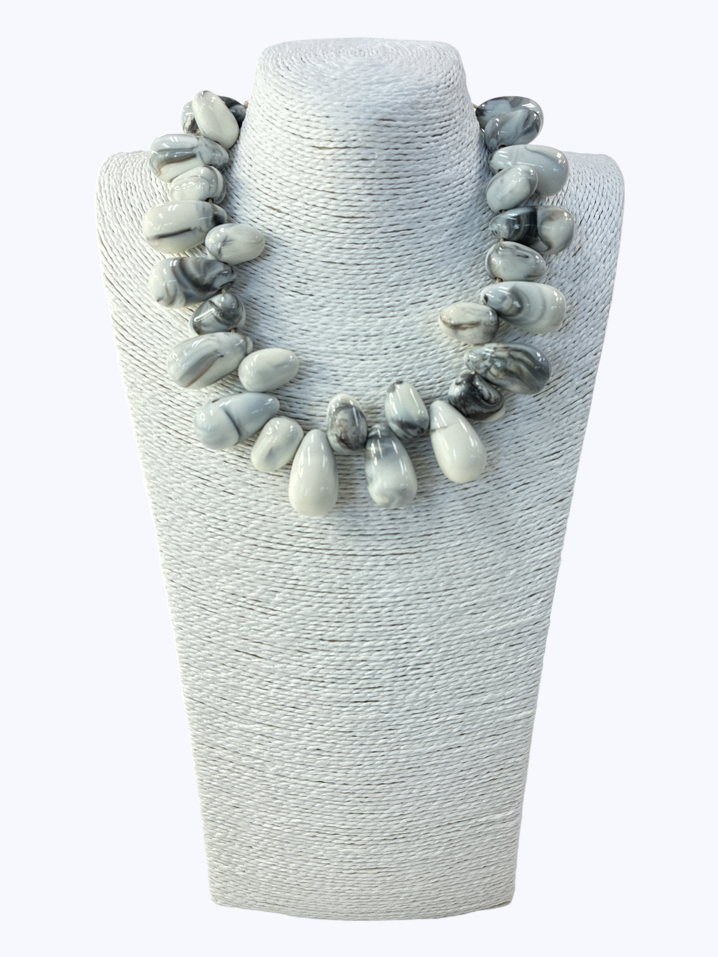 Necklace with gray and white stones on a textured white stand