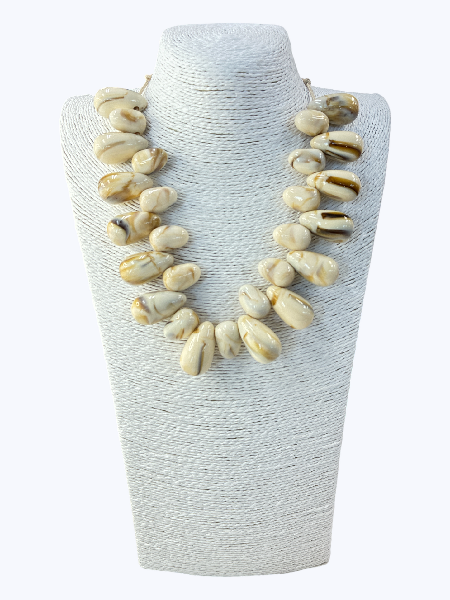 Shell necklace on a textured white stand against a white background