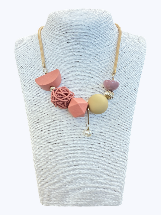 Abstract blush pink statement necklace with mixed geometric beads, woven accent detail, and pearl charm on gold-tone cord for a playful boutique-inspired look.
