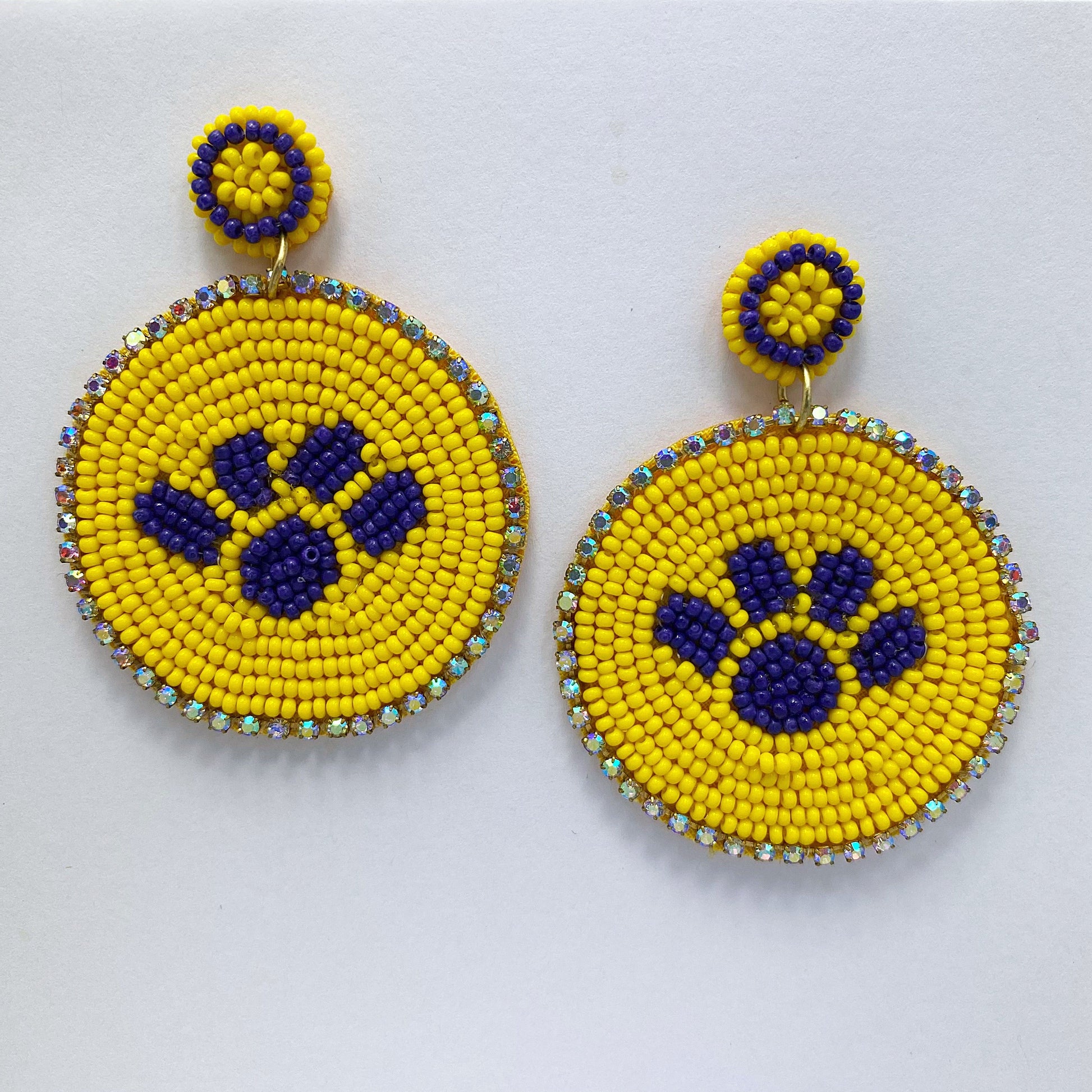 A pair of round yellow and blue beaded earrings with a geometric animal paw pattern and dangle post design.