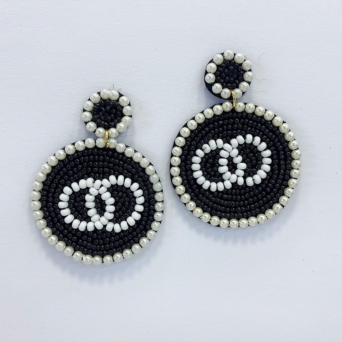 A pair of dangle post earrings with a geometric circle shape, featuring a mix of black and white beads and pearls.
