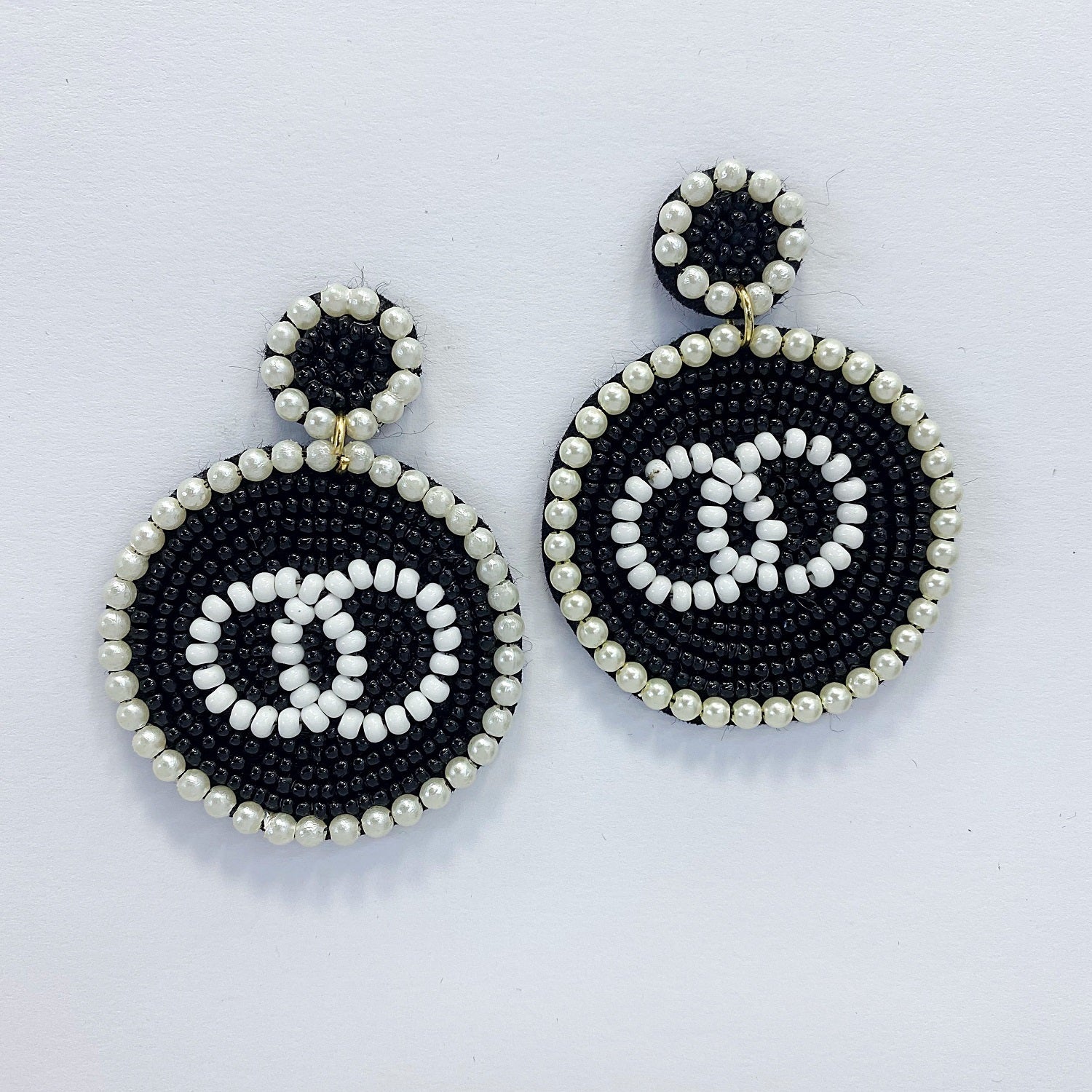 A pair of dangle post earrings with a geometric circle shape, featuring a mix of black and white beads and pearls.