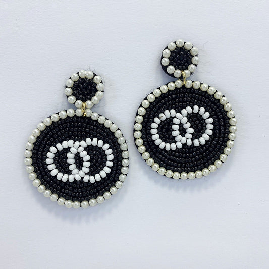 A pair of dangle post earrings with a geometric circle shape, featuring a mix of black and white beads and pearls.