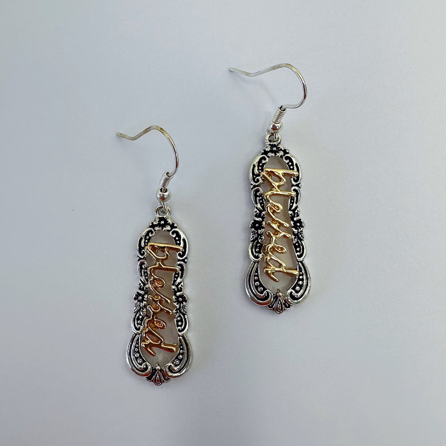 A pair of dangle hook earrings with a filigree design and the word 'blessed' in the center, featuring a black and white color scheme.