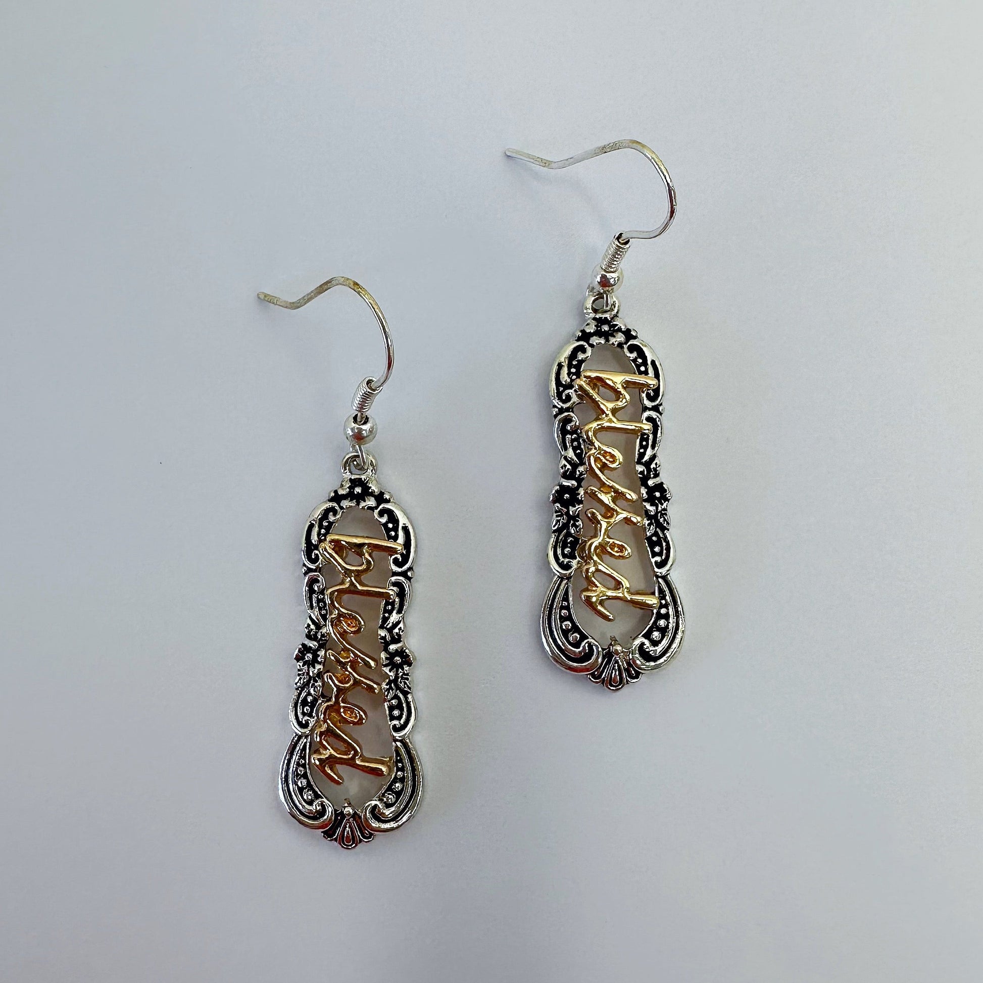 A pair of dangle hook earrings with a filigree design and the word 'blessed' in the center, featuring a black and white color scheme.
