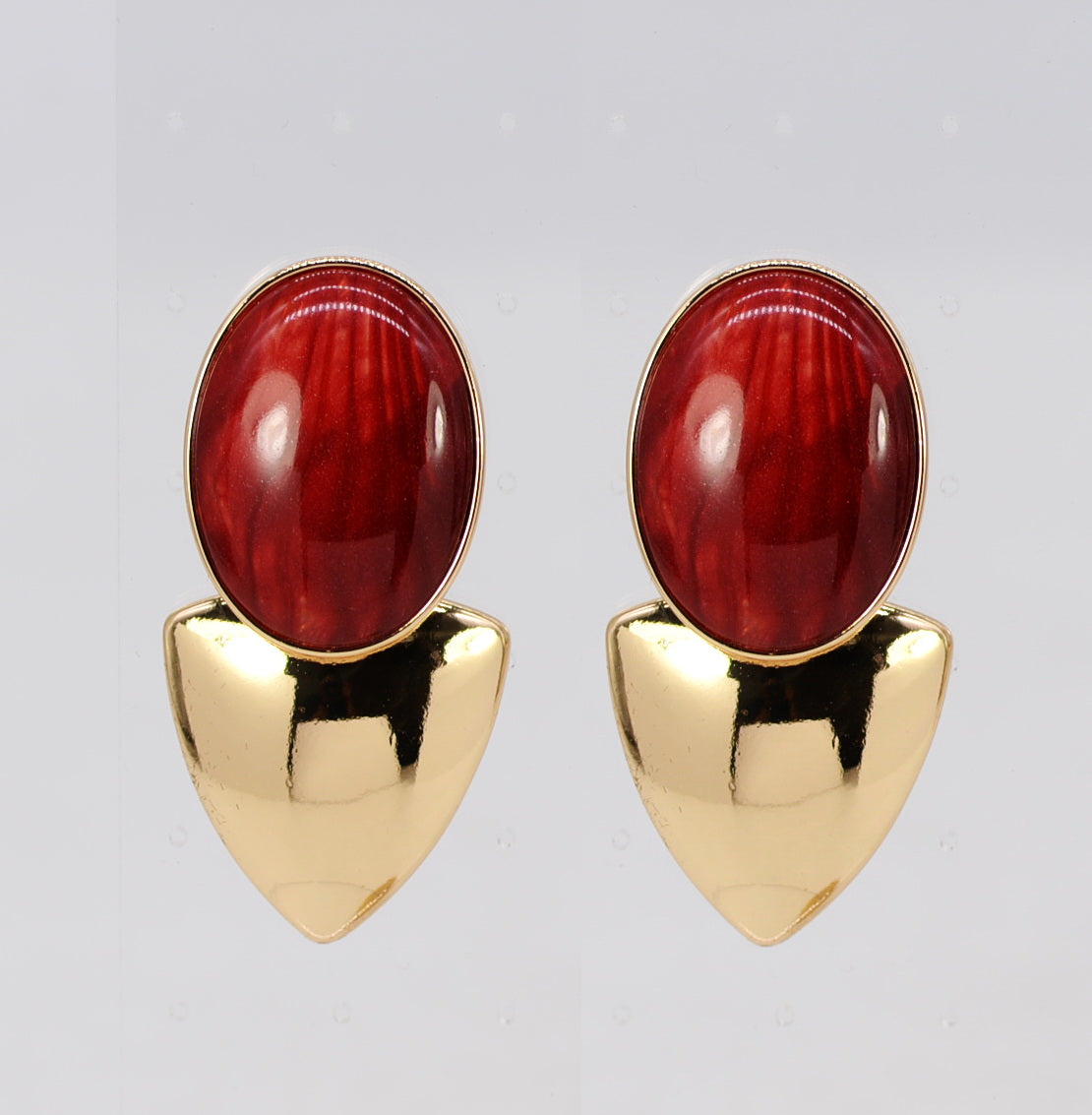 Pair of earrings with red stone and gold base on a light gray background