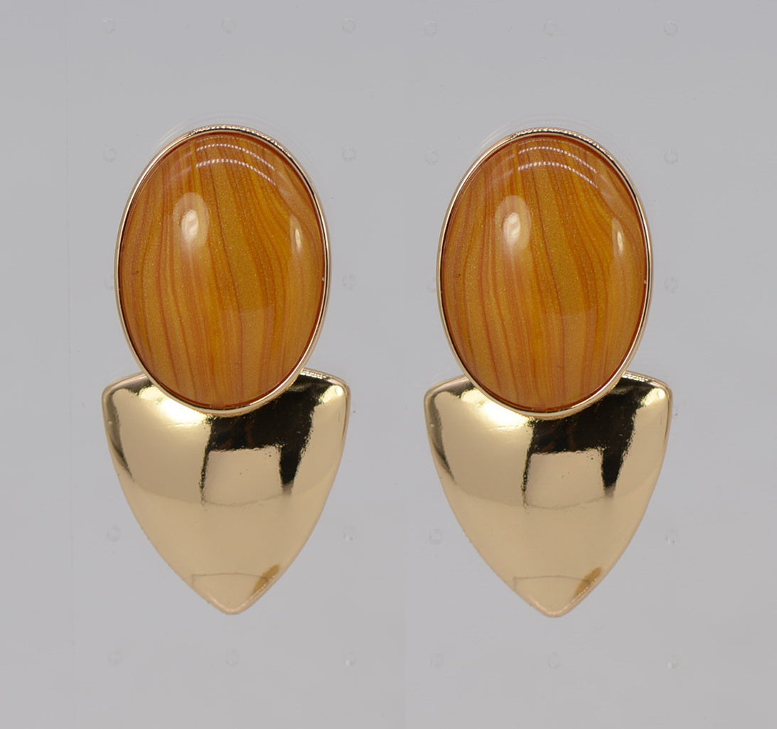 Gold earrings with orange stone on a gray background