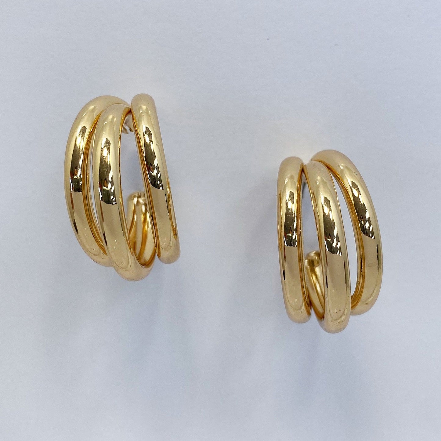 A pair of metal hoop earrings displayed in two colors, gold and silver, on a mannequin ear.