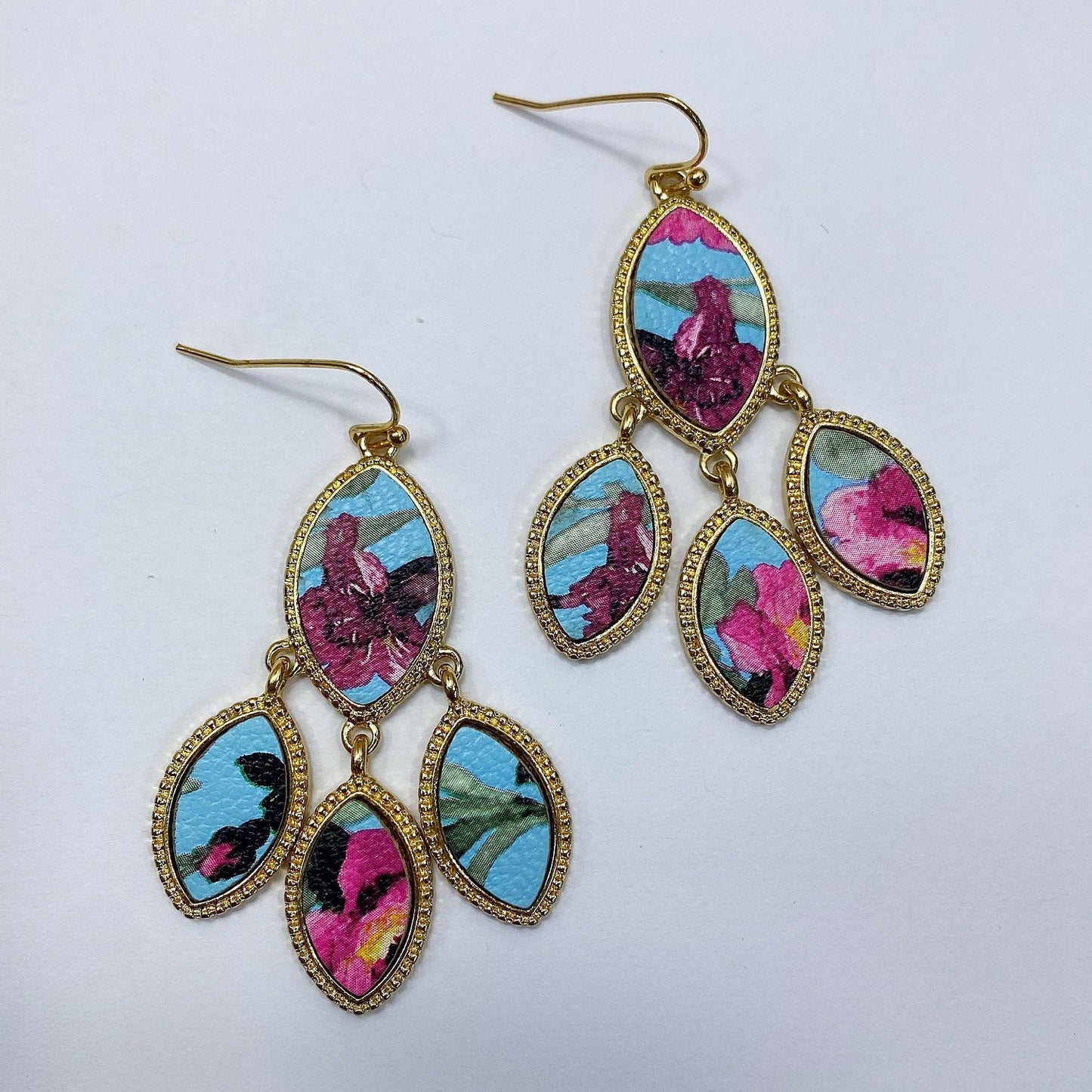 A pair of faux leather earrings with a floral pattern in colors pink, purple, and green, featuring gold-colored accents and hooks.