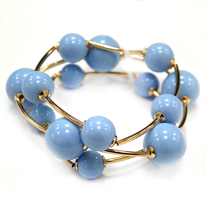 Layered coil bracelet with glossy round beads and gold tone curved metal accents in a modern wrap design.