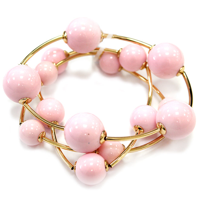 Layered coil bracelet with glossy round beads and gold tone curved metal accents in a modern wrap design.