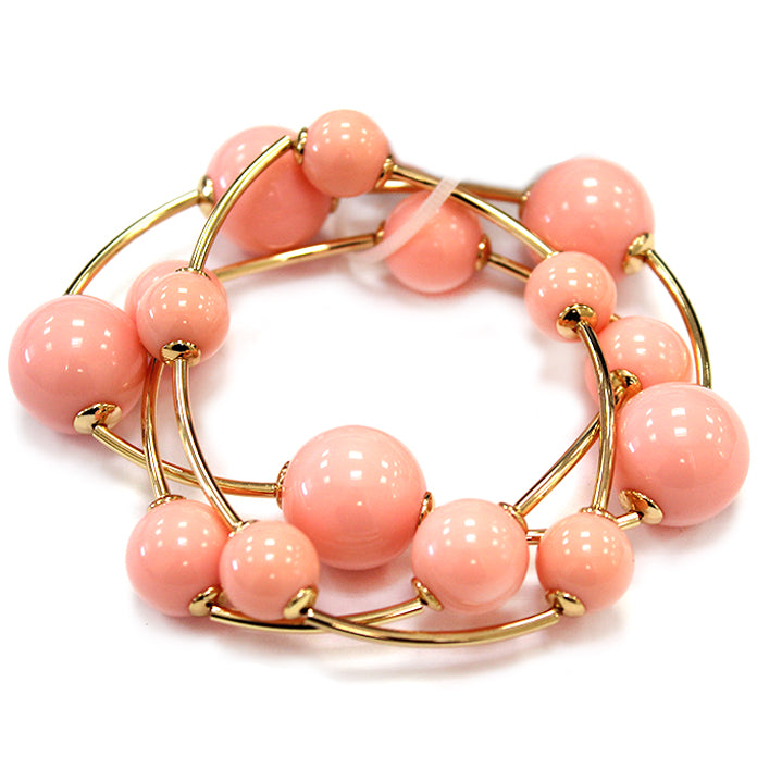 Layered coil bracelet with glossy round beads and gold tone curved metal accents in a modern wrap design.