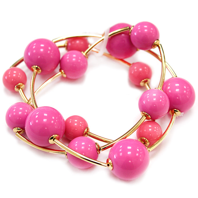Layered coil bracelet with glossy round beads and gold tone curved metal accents in a modern wrap design.