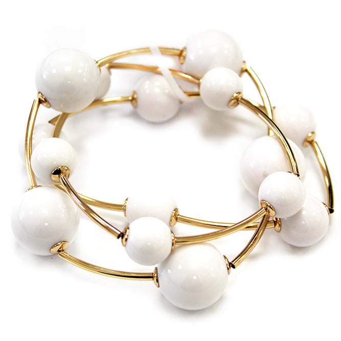 Layered coil bracelet with glossy round beads and gold tone curved metal accents in a modern wrap design.