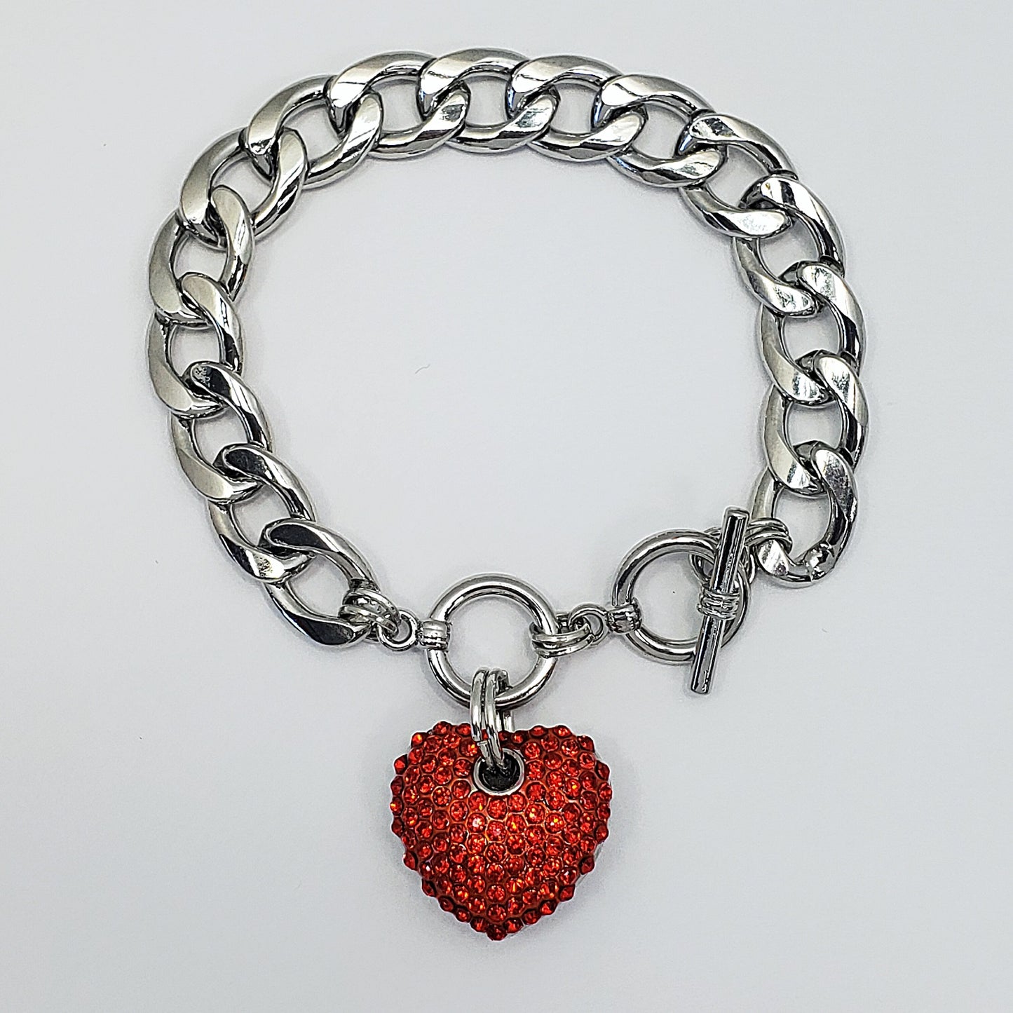 Silver chain bracelet with a red heart charm on a light gray background