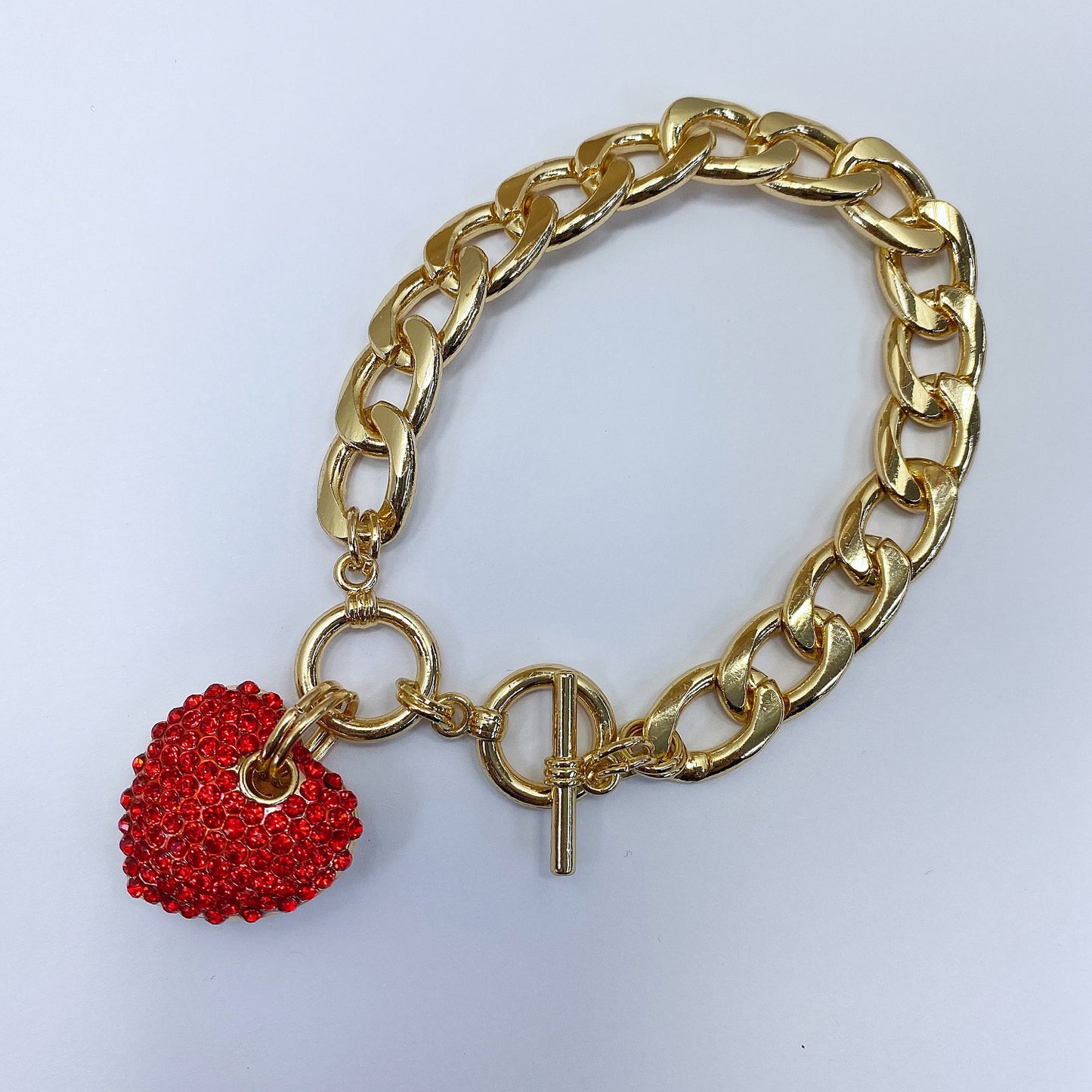Gold chain bracelet with a red heart charm on a white background
