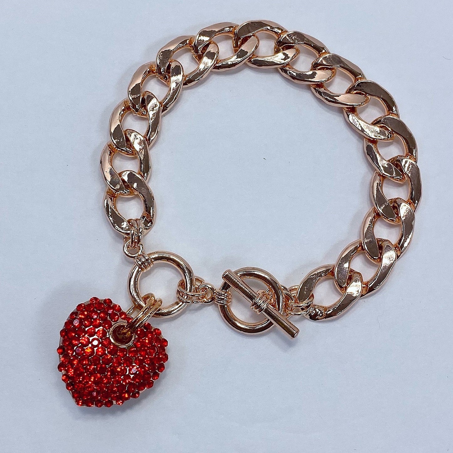 Rose gold chain bracelet with a red heart charm on a light gray background