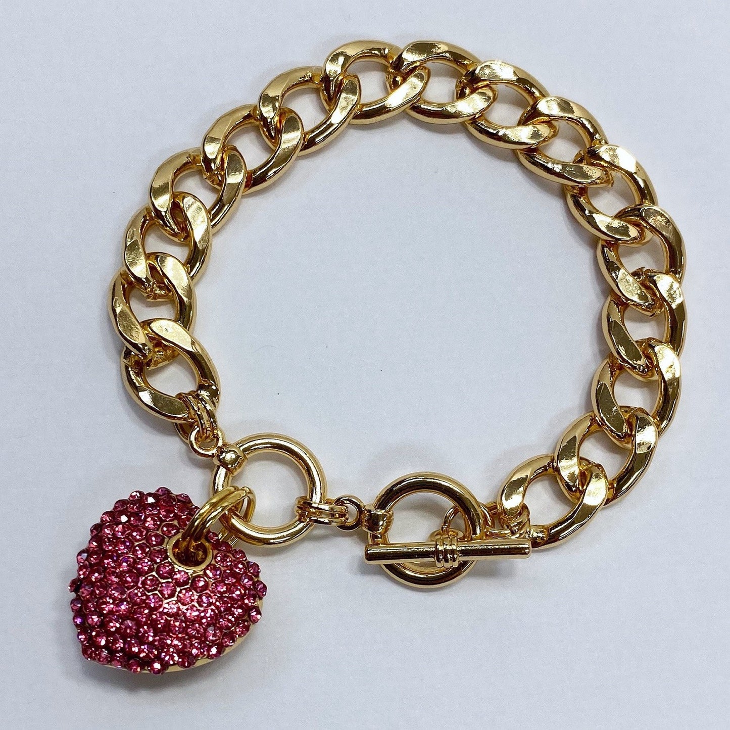 Gold chain bracelet with a pink heart charm on a white background