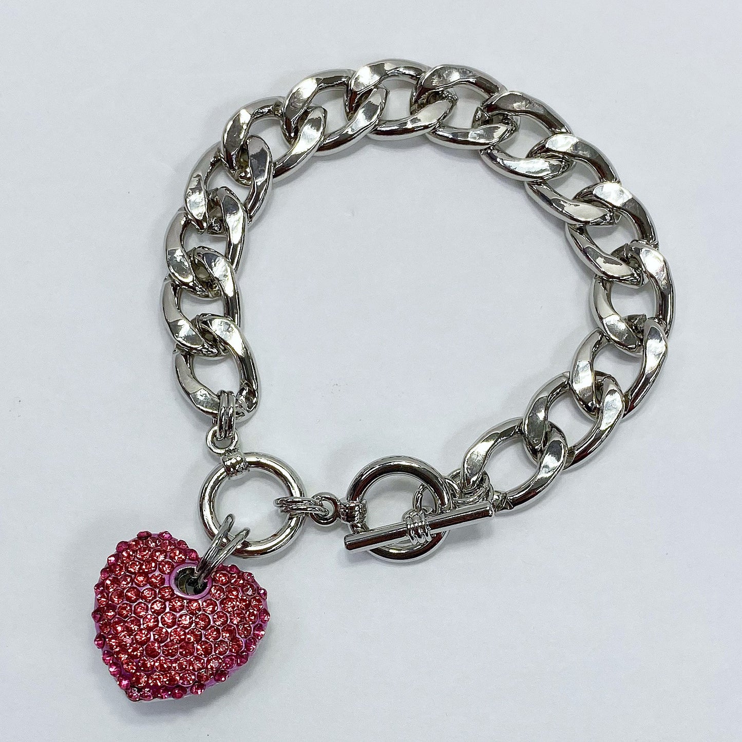 Silver chain bracelet with a pink heart charm on a light gray background