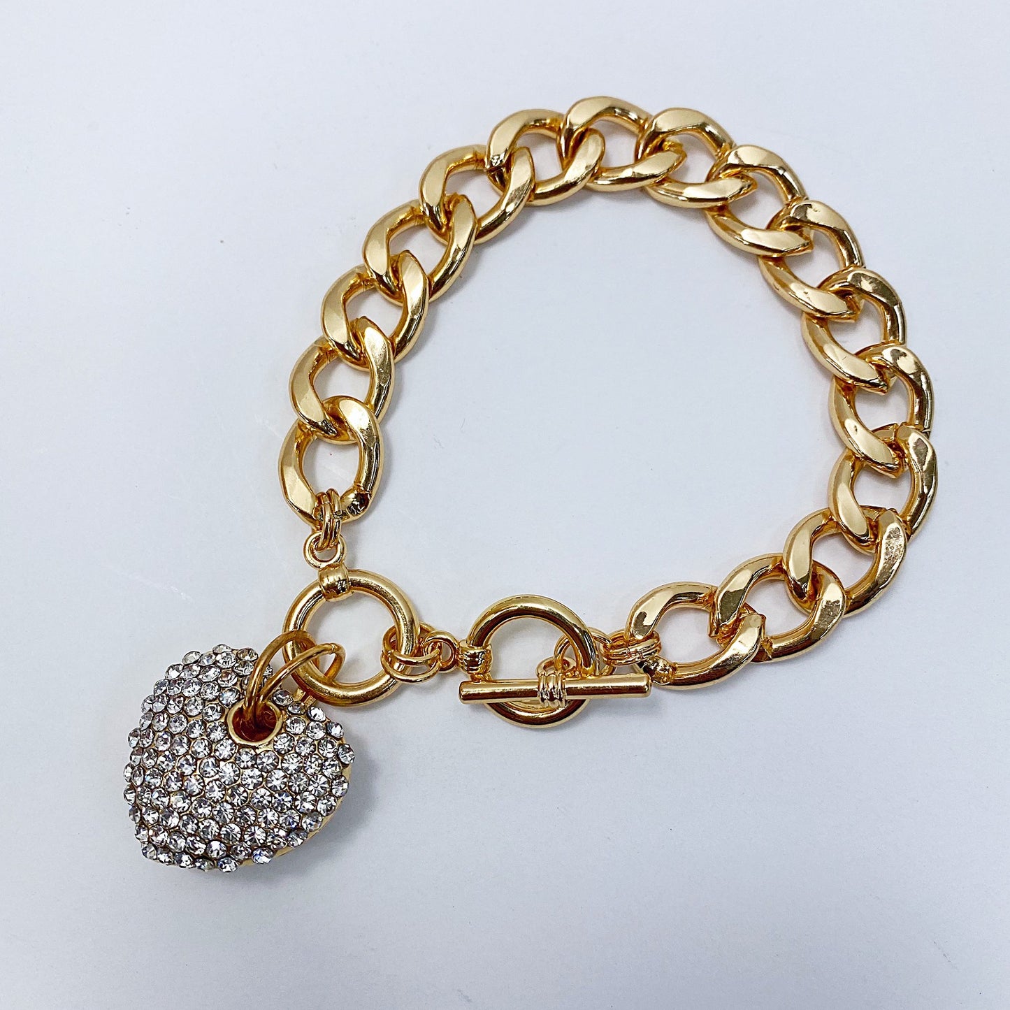 Gold chain bracelet with a heart-shaped charm on a light gray background