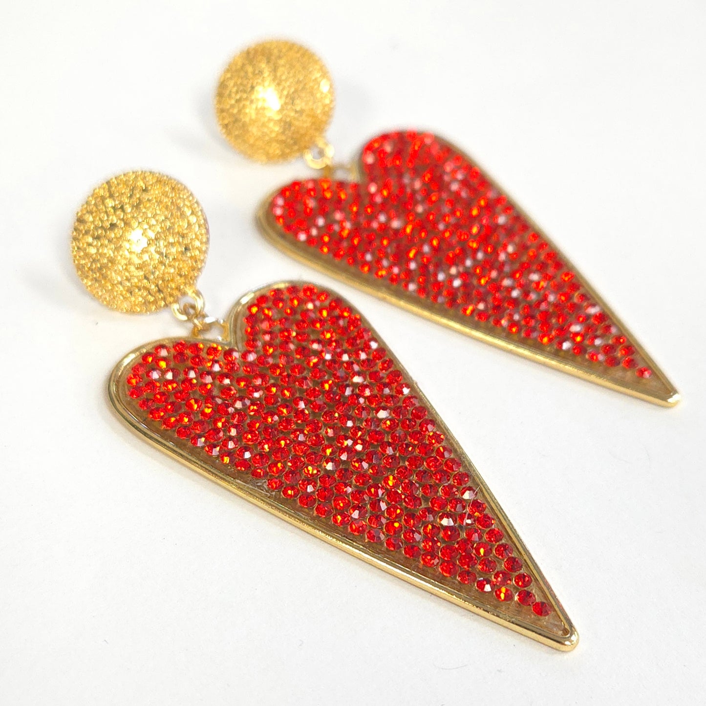 Heart-shaped earrings with red gemstones and gold accents on a white background