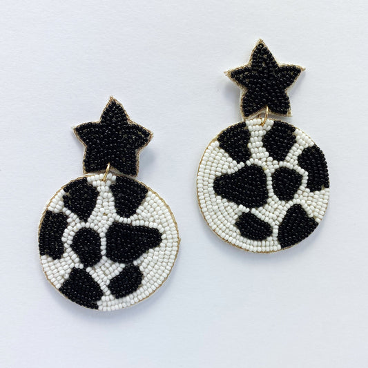 A pair of dangle hook earrings with a black and white cow pattern design and gold accents.