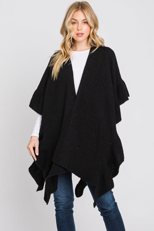 Woman wearing a black poncho over a white shirt and blue jeans on a light gray background