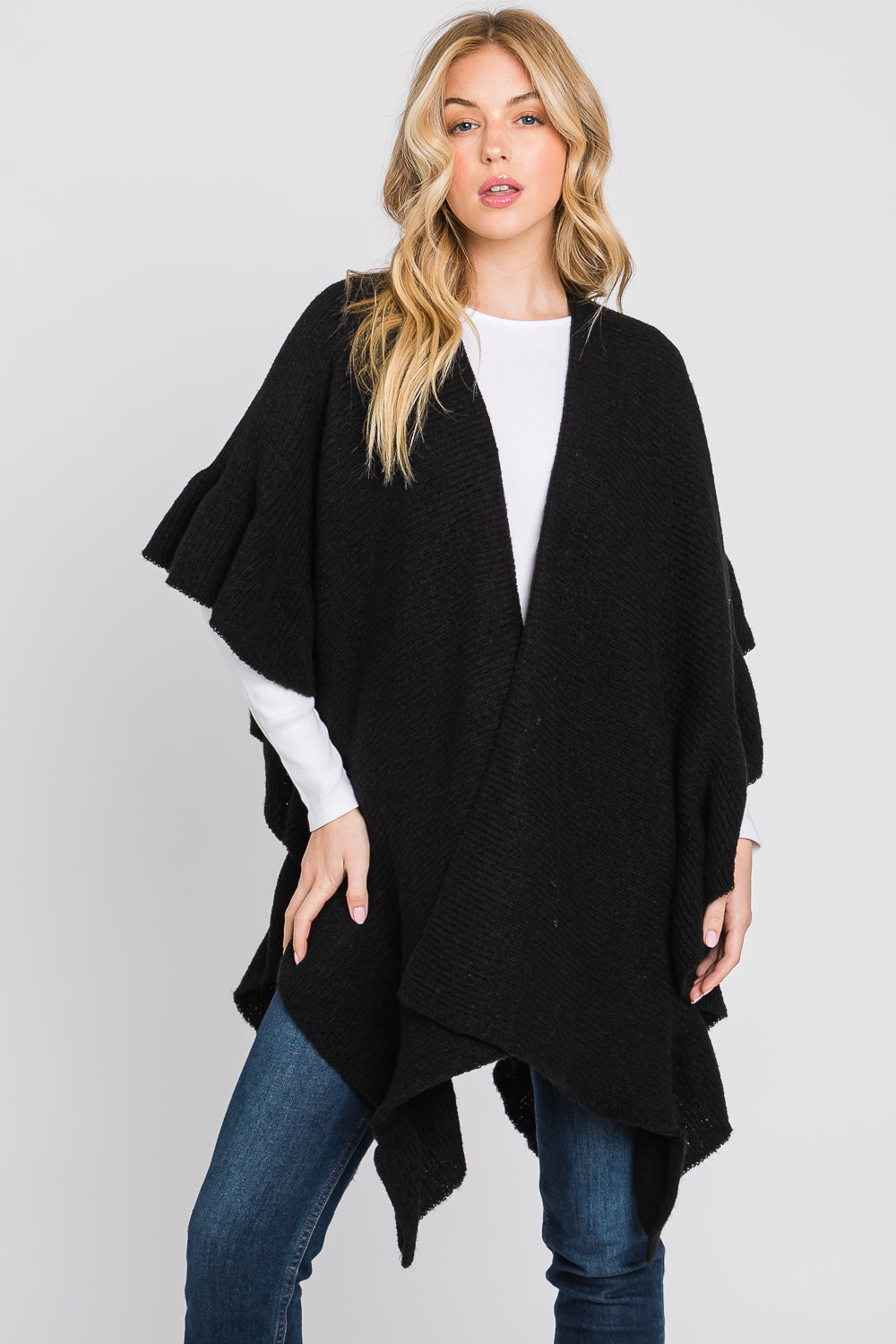Woman wearing a black poncho over a white top and blue jeans on a white background