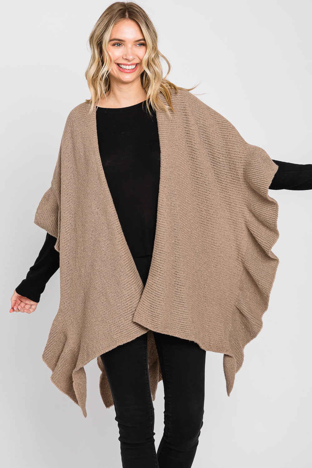 Woman wearing a beige poncho over a black outfit on a white background