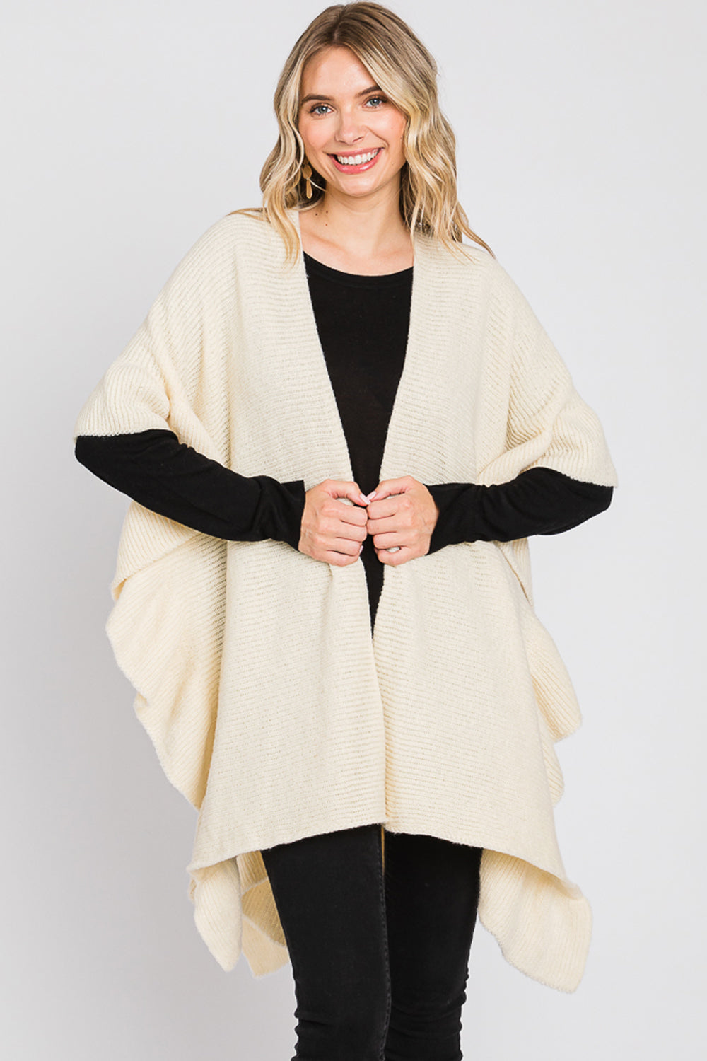 Woman wearing a beige poncho with black cuffs on a white background