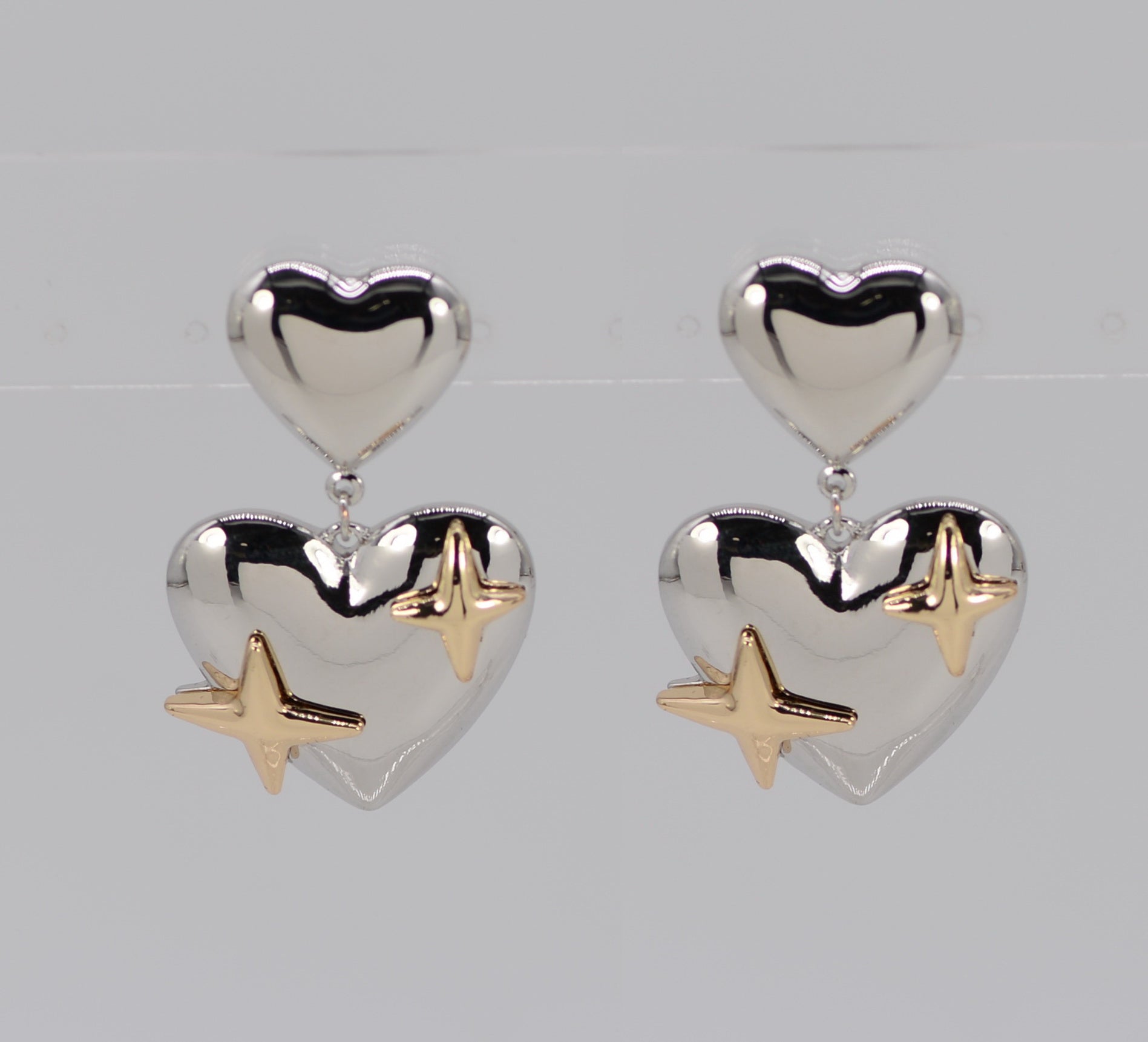 Heart-shaped earrings with gold star accents on a light gray background