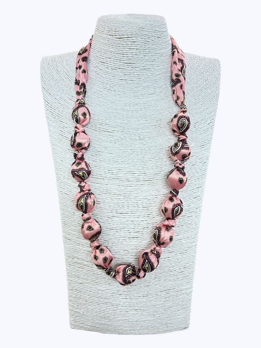 Necklace with pink and black patterned beads on a light gray stand against a white background