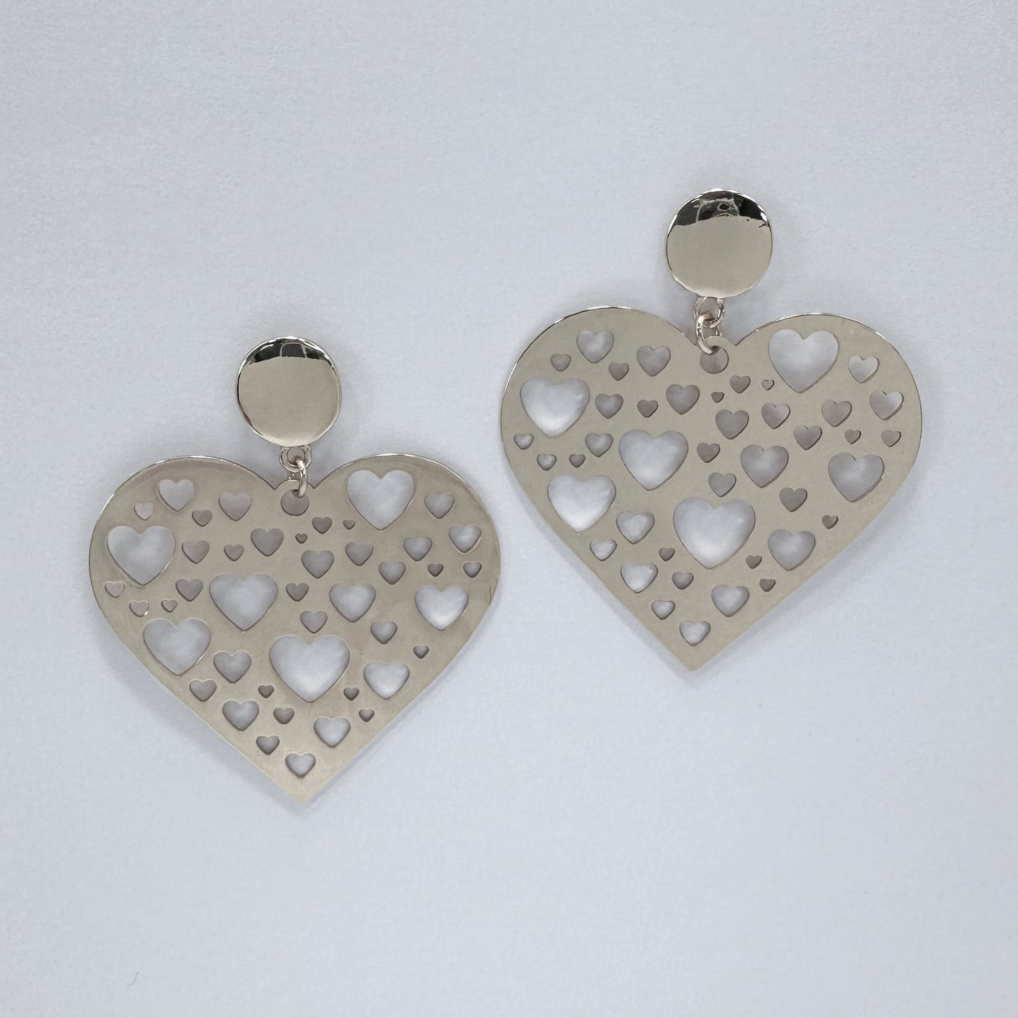 Heart-shaped earrings with cut-out designs on a light gray background
