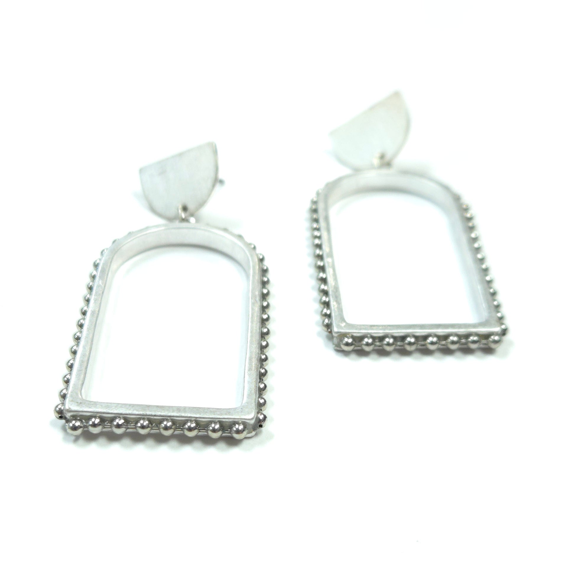 Pair of silver square earrings with white stones on a white background