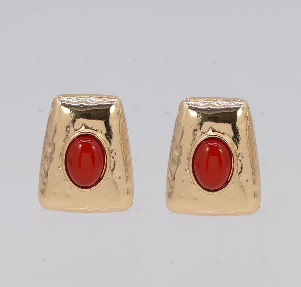 Pair of gold earrings with red stones on a gray background