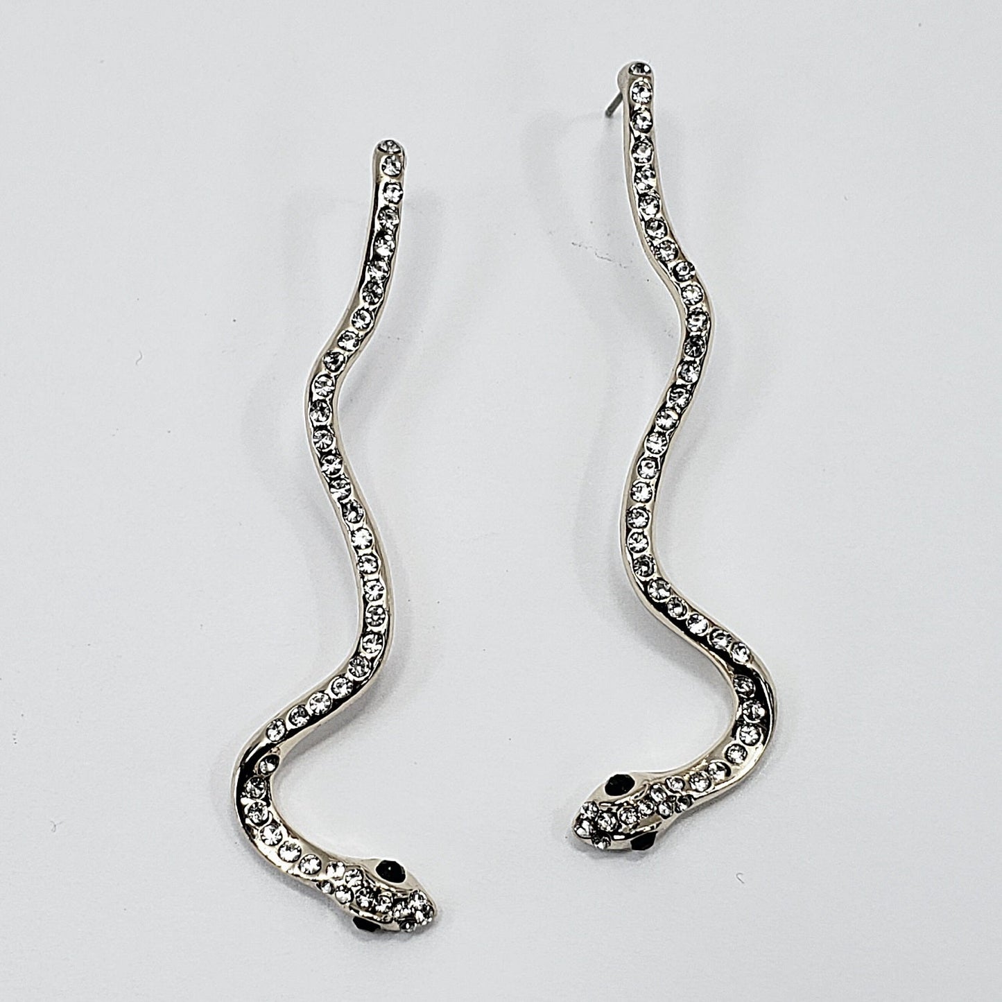 A pair of silver serpent earrings on a white background
